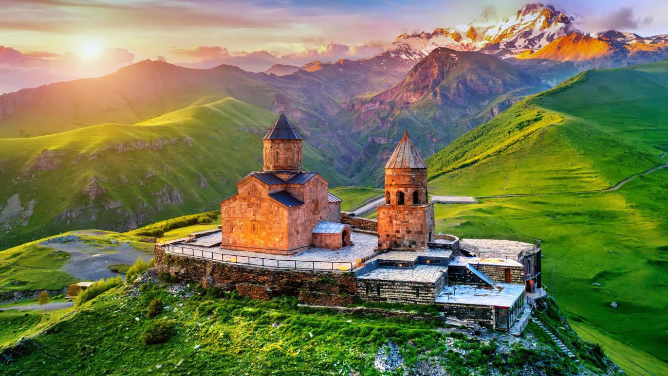 View of Gergeti Trinity Church in Kazbegi, Georgia during sunrise with mountains in background