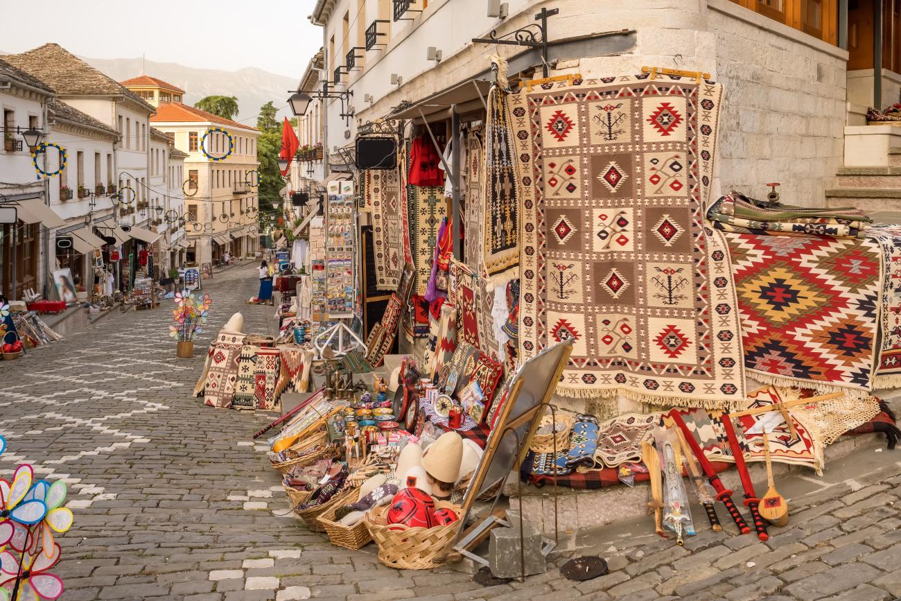 Exterior of a souvenir shop with carpets and various souvenirs with a cobbled street in the background